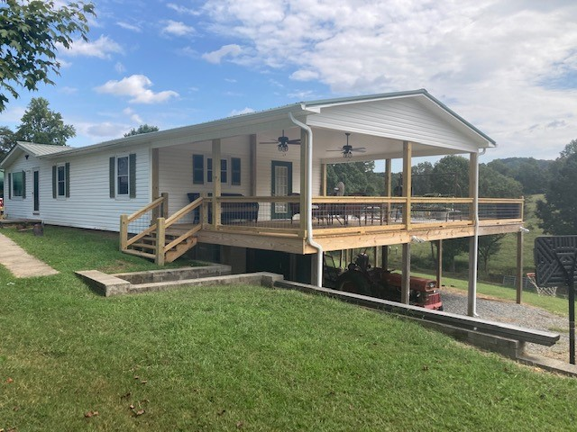 A large, elevated covered back porch and deck addition on a white siding home, featuring natural wood columns, custom railings and ceiling fans.